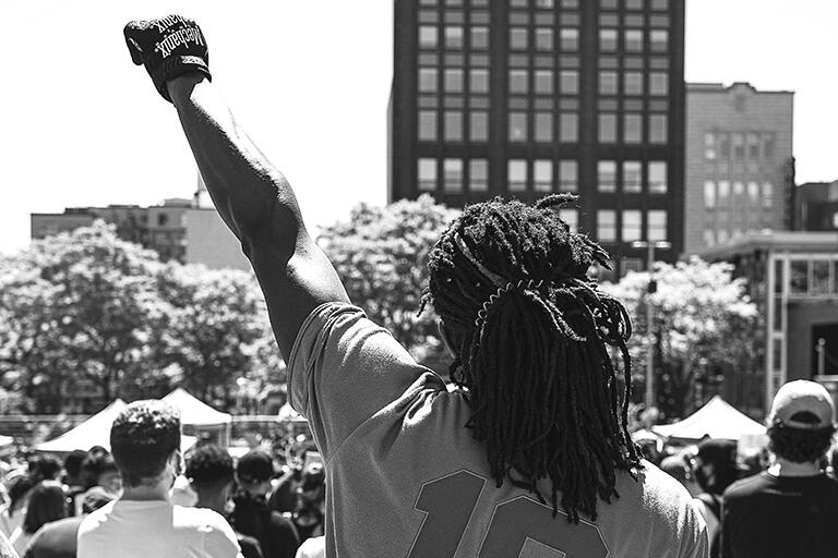 back view of man with dreads wearing sports jersey with fist raised in BLM salute
