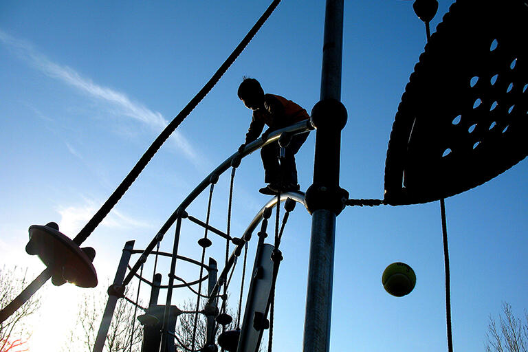 child on play structure silhouetted against sky