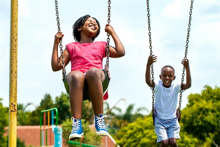 smiling Black girl and boy playing on swingset