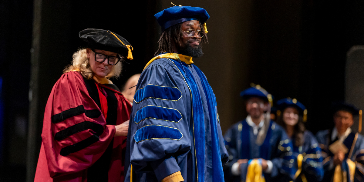 PhD graduate getting hooded at commencement ceremony by faculty advisor