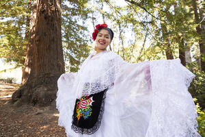 Graciela Ruiz in folklórico dress standing in front of redwood tree