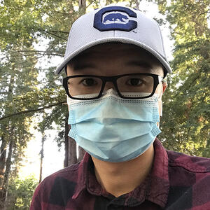 MSW student David Pan wearing a mask and a Cal hat with trees in the background