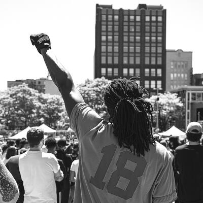 man with dreads seen from back wearing sports jersey and giving Black Power salute
